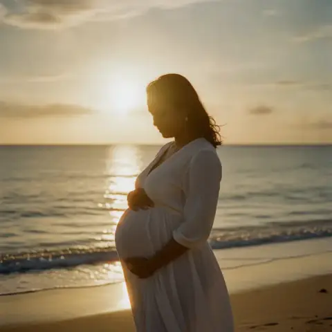 Future maman en robe claire sur une plage au coucher du soleil